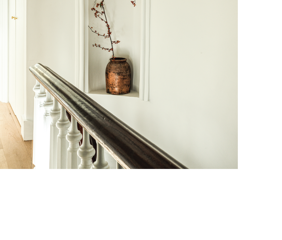 A softly lit niche with a single branch in an antique vessel above a painted stair rail