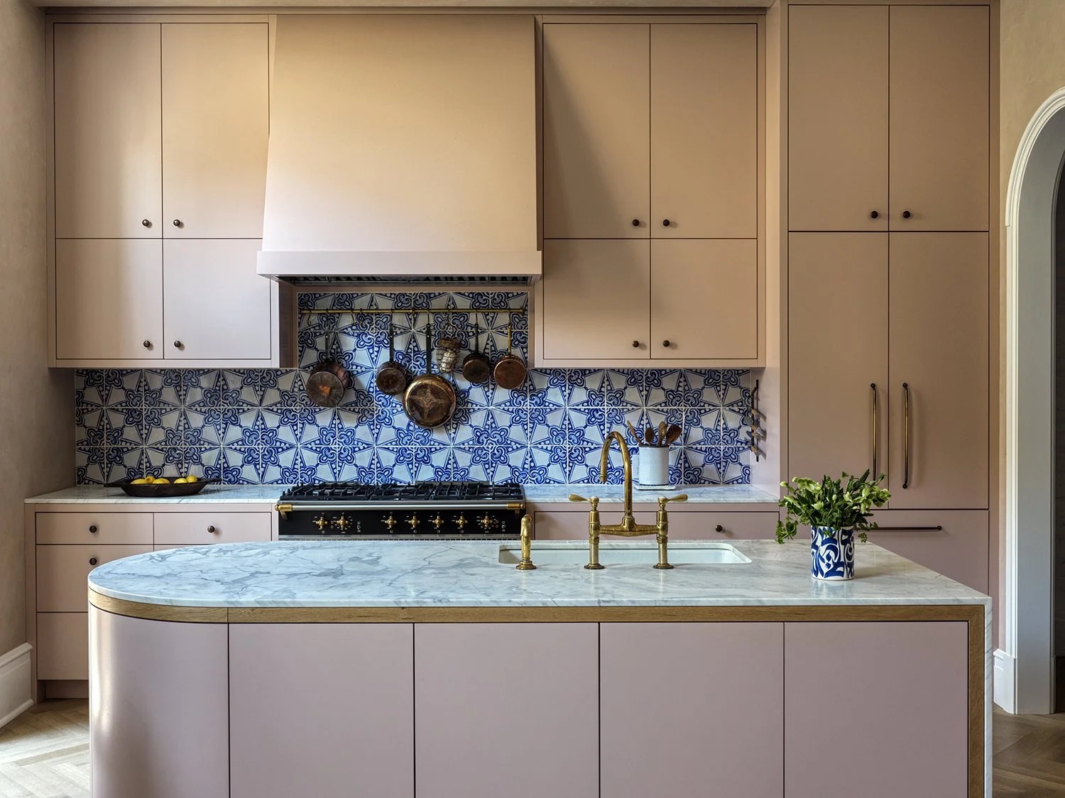 A blush pink kitchen with hand-painted blue tile backsplash and marble island, designed by Hallie Goodman