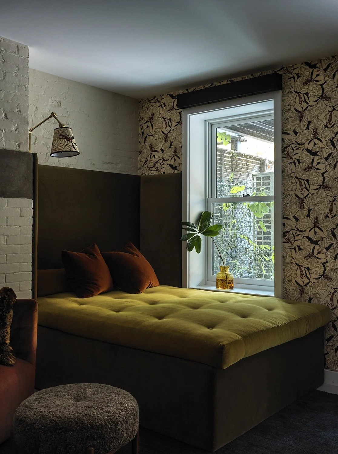 A moody bedroom lounge with olive velvet bed, botanical wallpaper and terracotta pillows