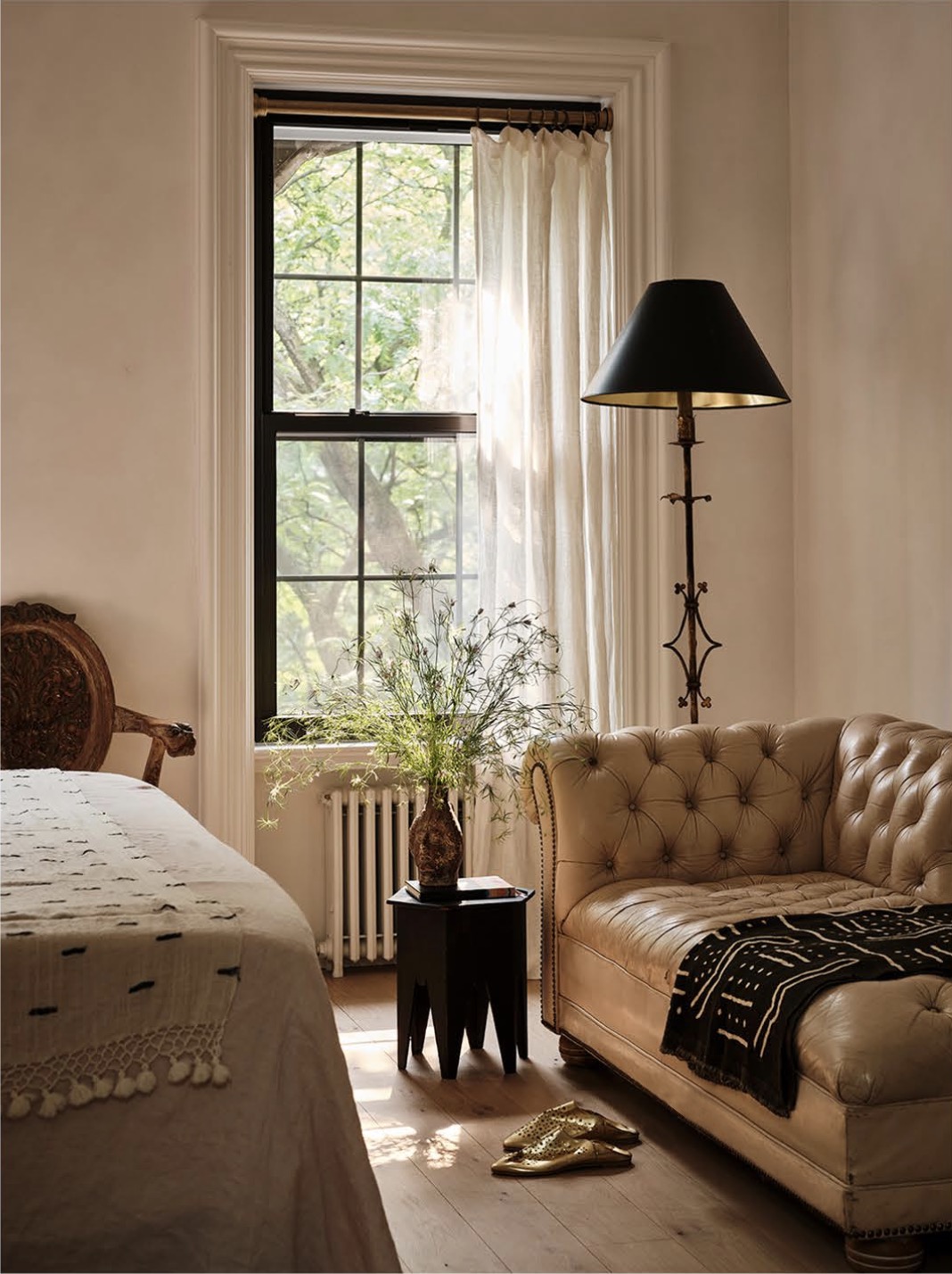 A serene bedroom with a tufted settee, black shaded lamp and soft natural light